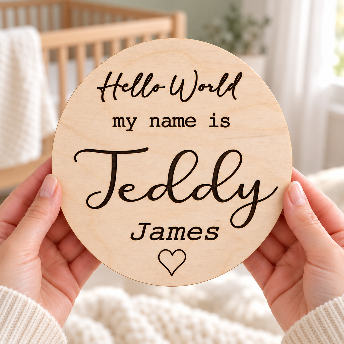 Birth announcement sign held in hands in a bright nursery, engraved Hello World my name is Teddy James with a heart