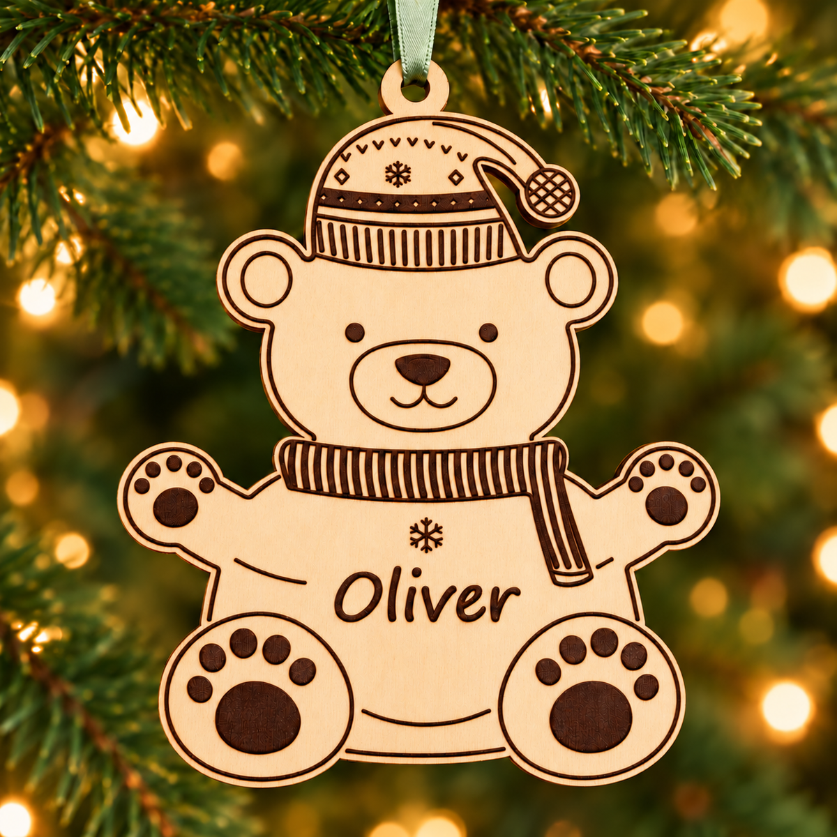 Personalised wooden polar bear bauble engraved with Oliver, hanging on a Christmas tree from a sage green satin ribbon.