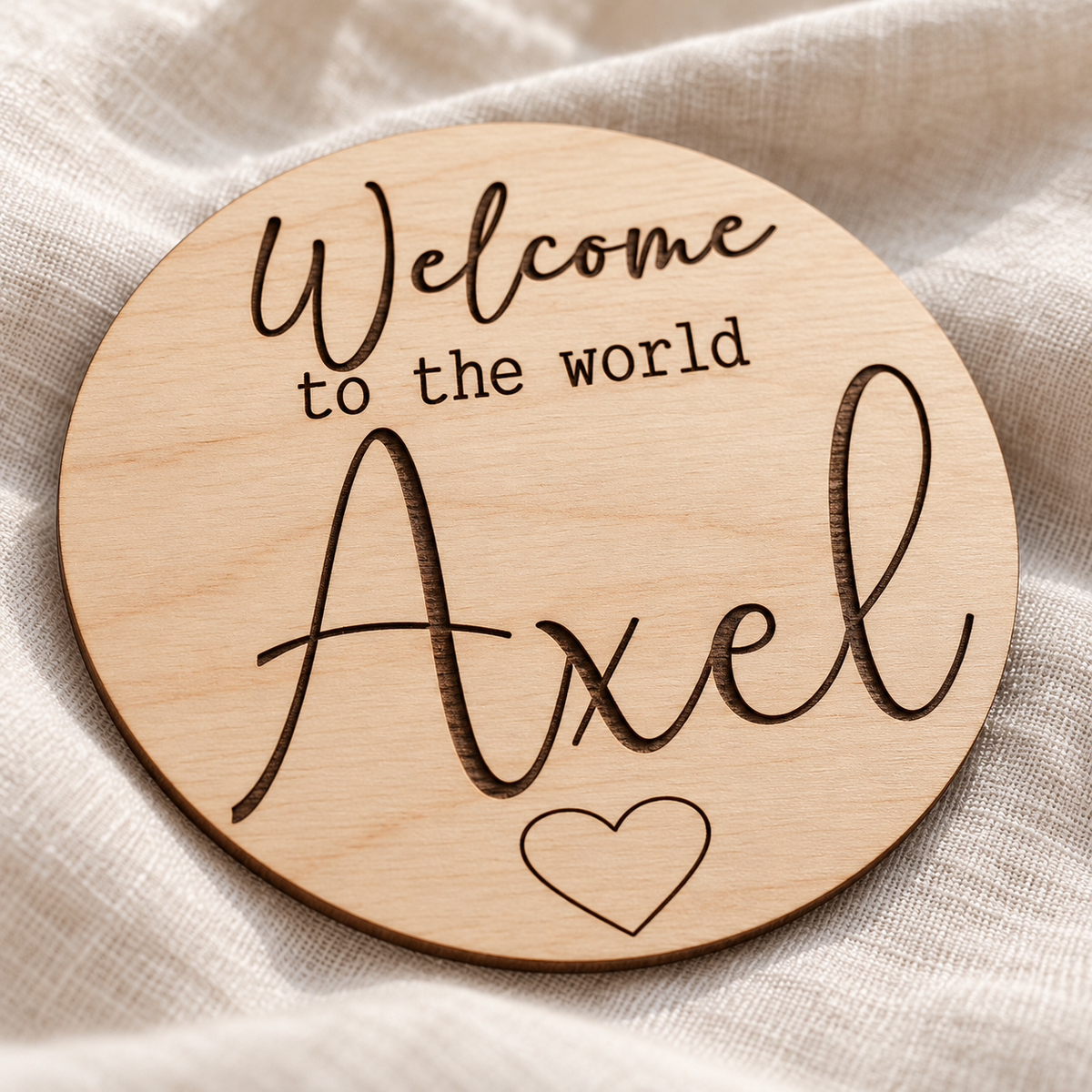 Close-up of the dark engraved Axel name and outline heart on the natural birch Welcome to the World sign