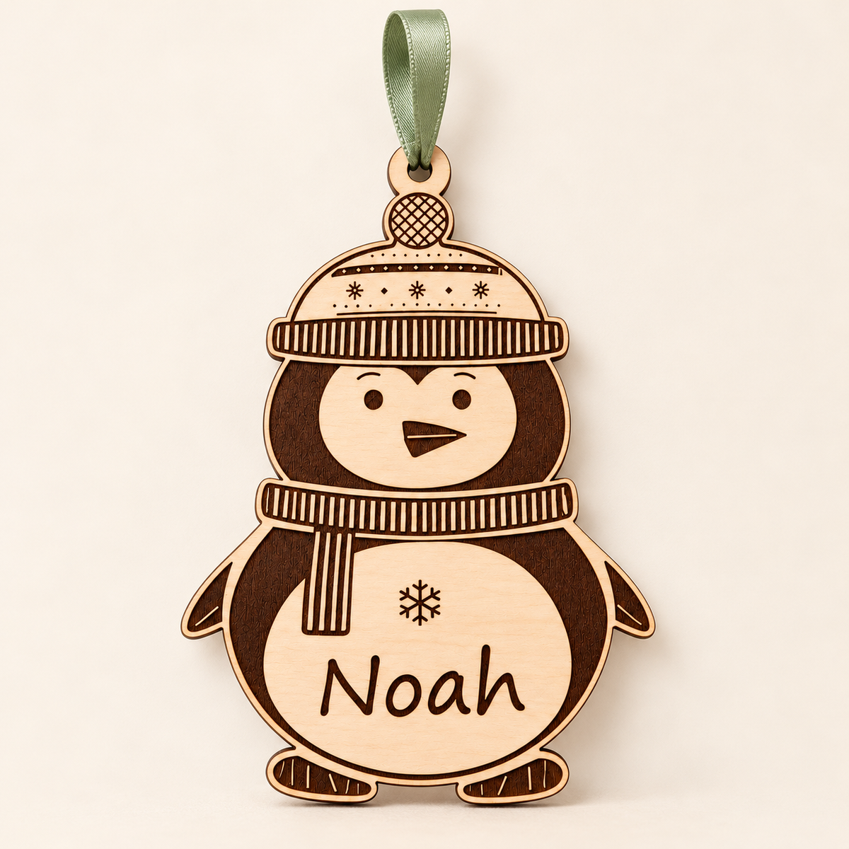 Full front view of a personalised penguin Christmas ornament with sage green ribbon against an ivory background