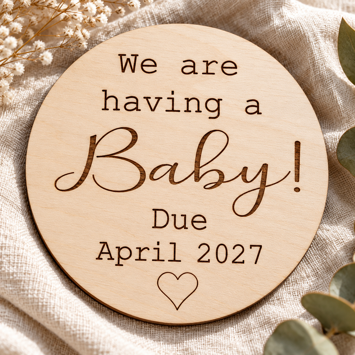 Close-up of dark espresso laser engraving and natural birch grain on a round pregnancy reveal plaque