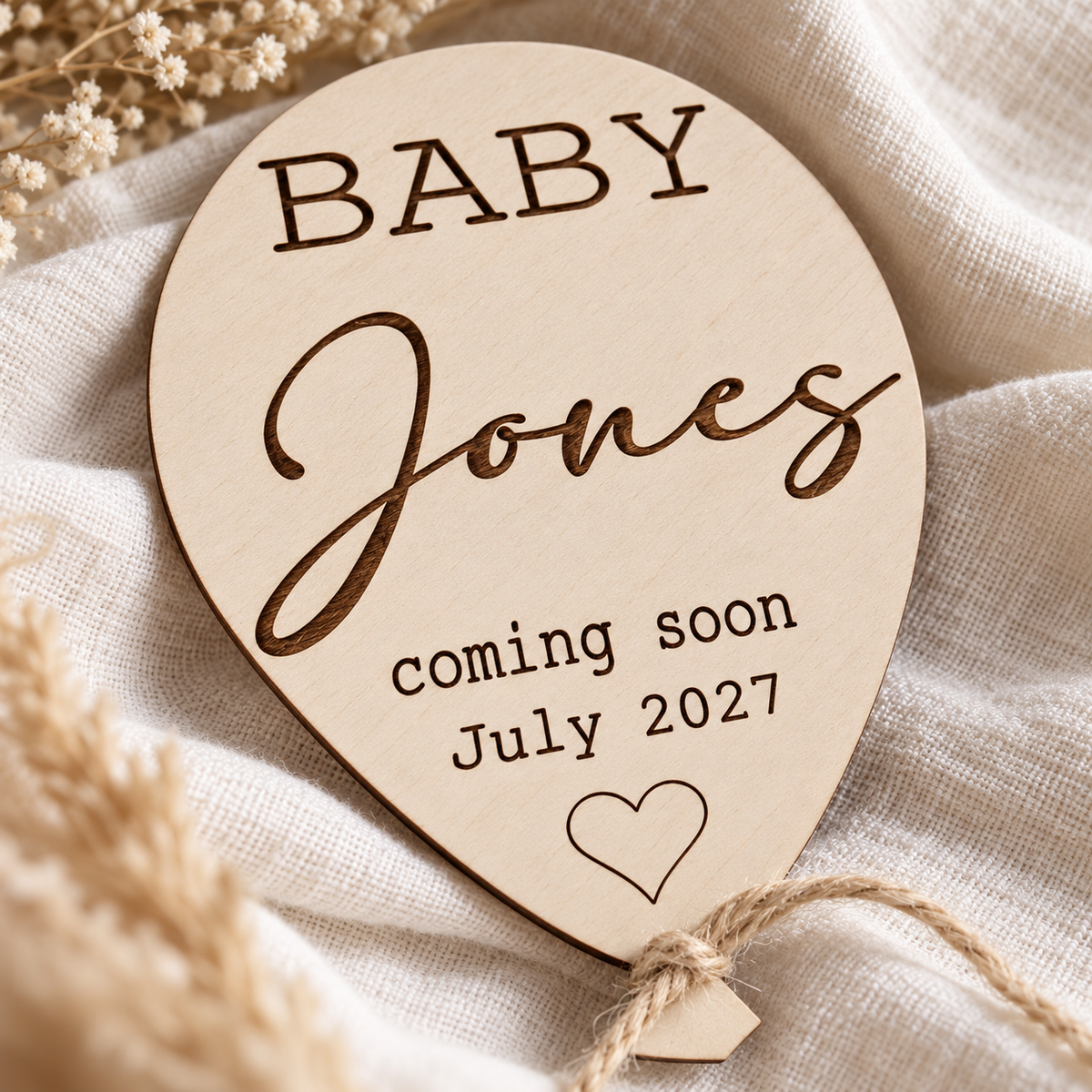 Close-up of dark surname and due date engraving on birch plywood balloon with jute string