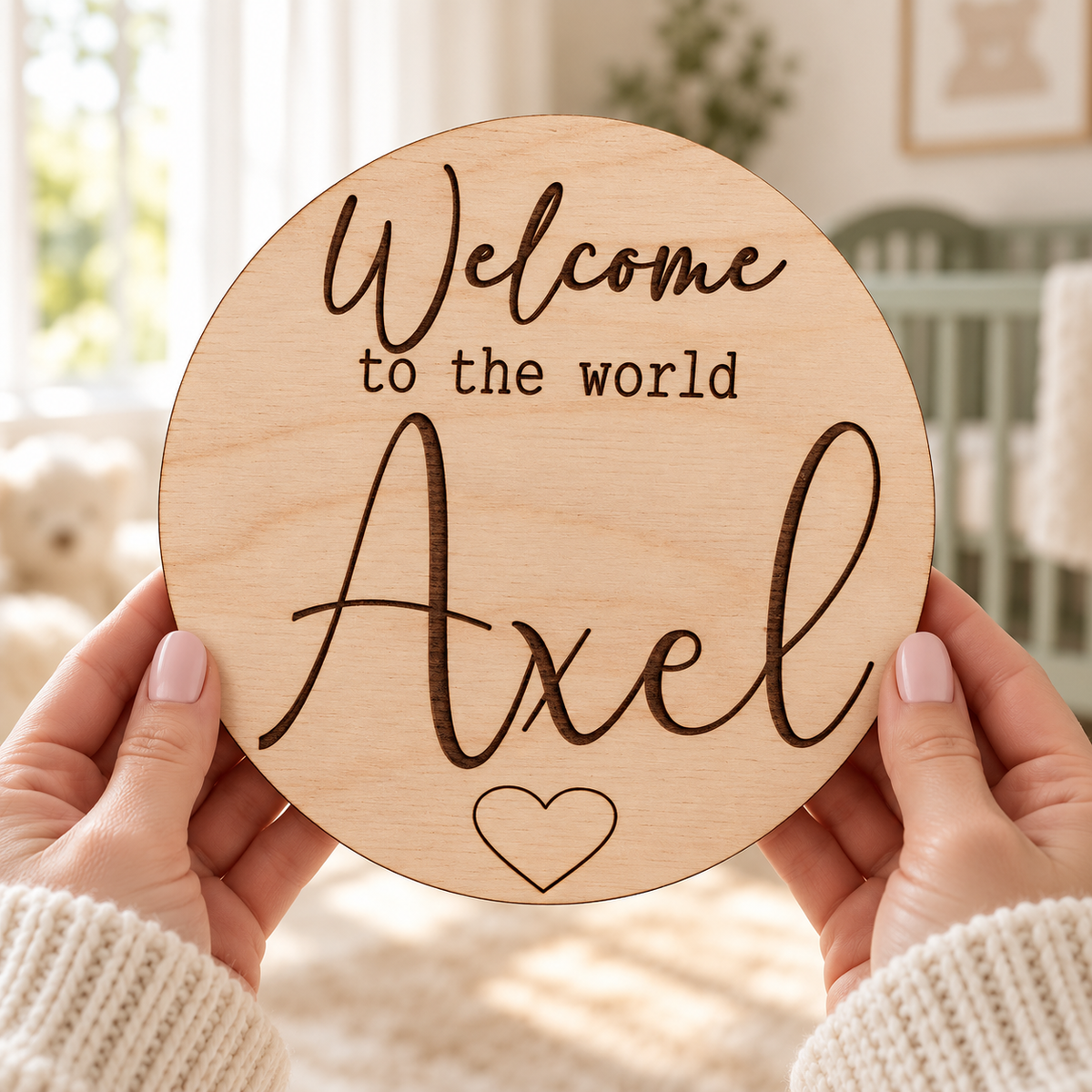 Hands holding the round Welcome to the World Axel sign in a bright nursery with dark brown-black engraving