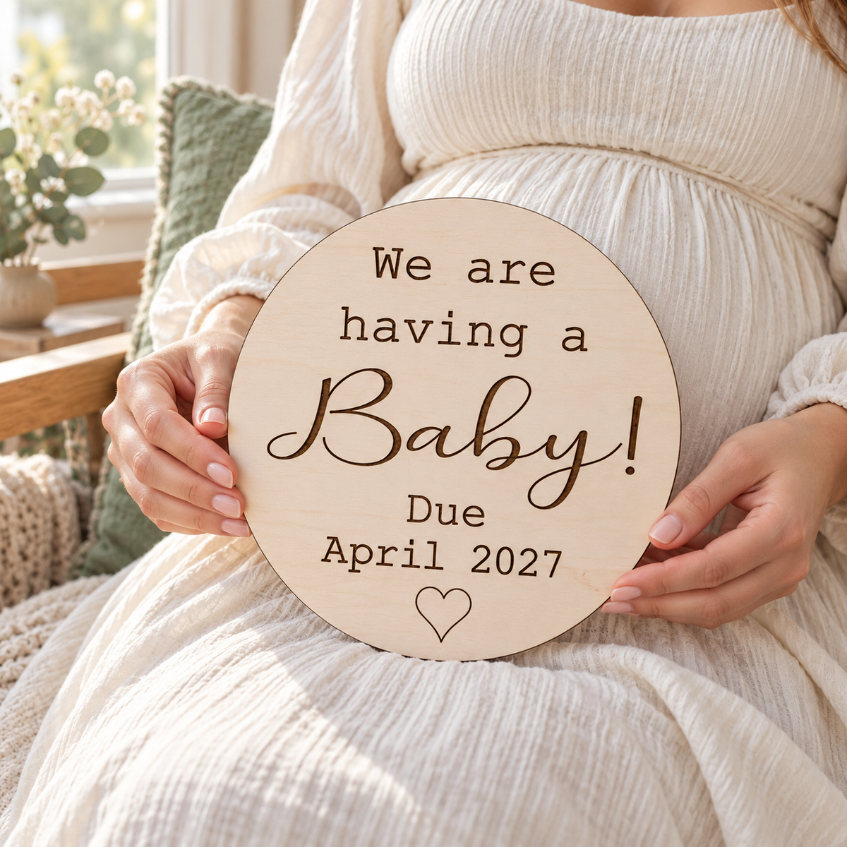 Expectant mother holding a round We are having a Baby due date plaque in front of her bump