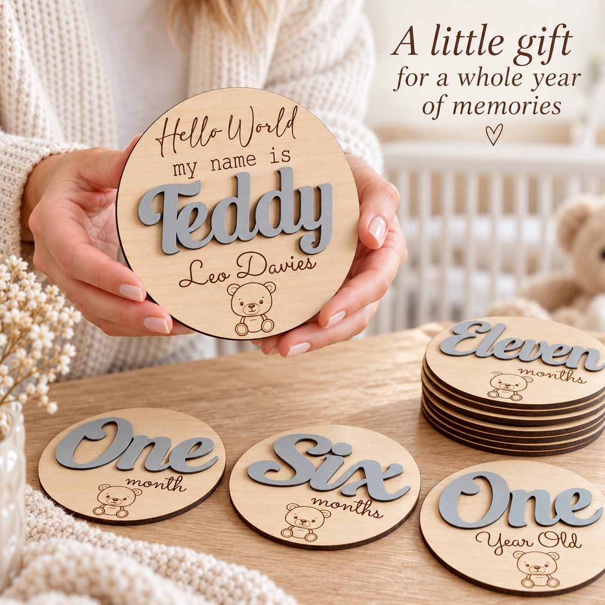 Parent holding Grey personalised name plaque above matching monthly milestone discs in a nursery.