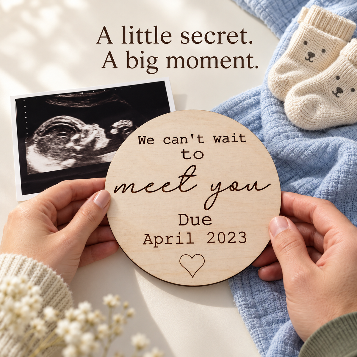 Hands holding a Can't Wait to Meet You pregnancy reveal plaque with ultrasound photo and small baby socks.