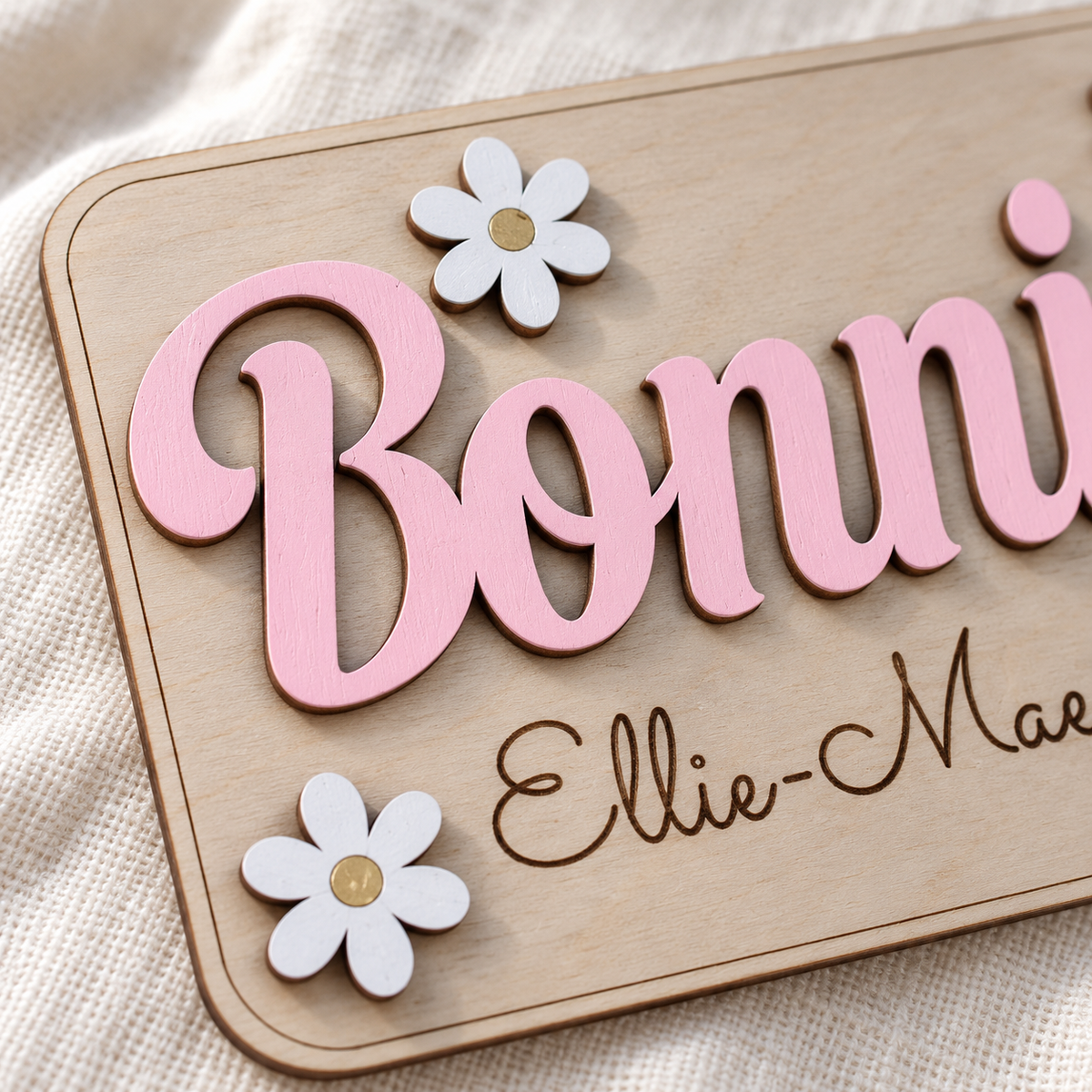 Close view of painted raised wooden lettering, dark engraved names and white daisies