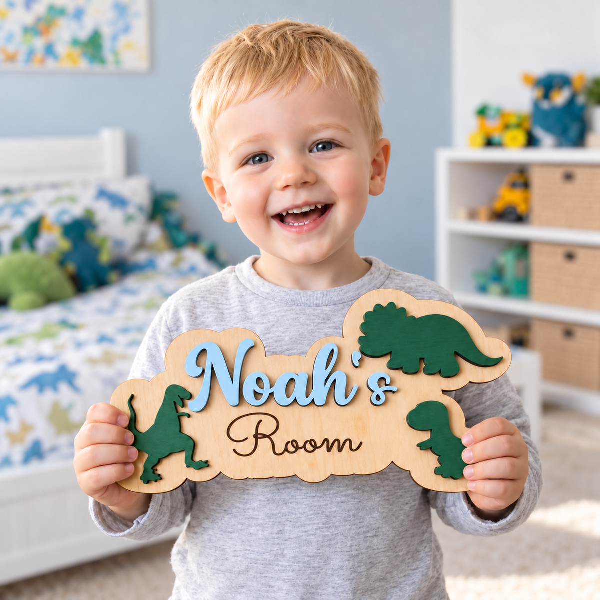 Child holding a personalised Noah's Room dinosaur sign with a true capital N in pastel blue lettering and three green dinosaurs.