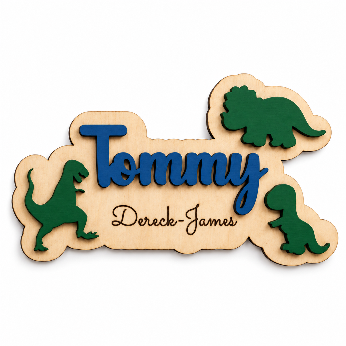 Close view of the navy Tommy dinosaur name plaque with natural birch backing, green dinosaurs and engraved Dereck-James on white.