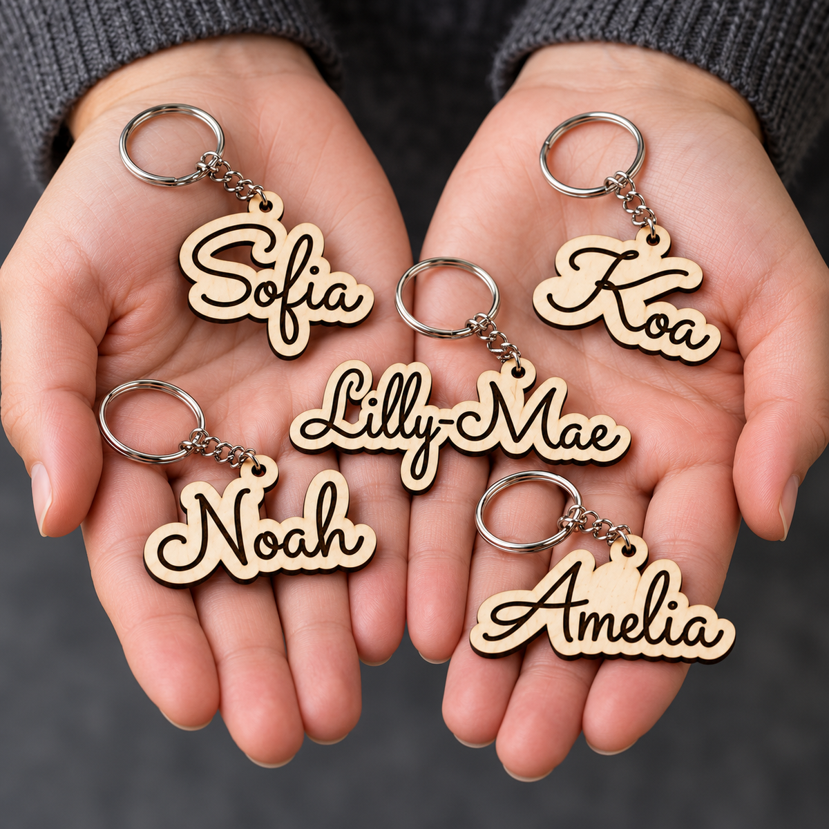Five personalised wooden keyrings held in hands, showing the names Sofia, Koa, Lilly-Mae, Noah and Amelia.