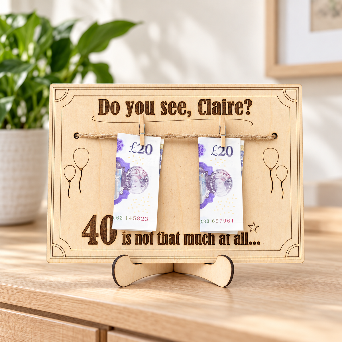 Funny personalised wooden birthday card and money holder displayed on its stand beside a green plant