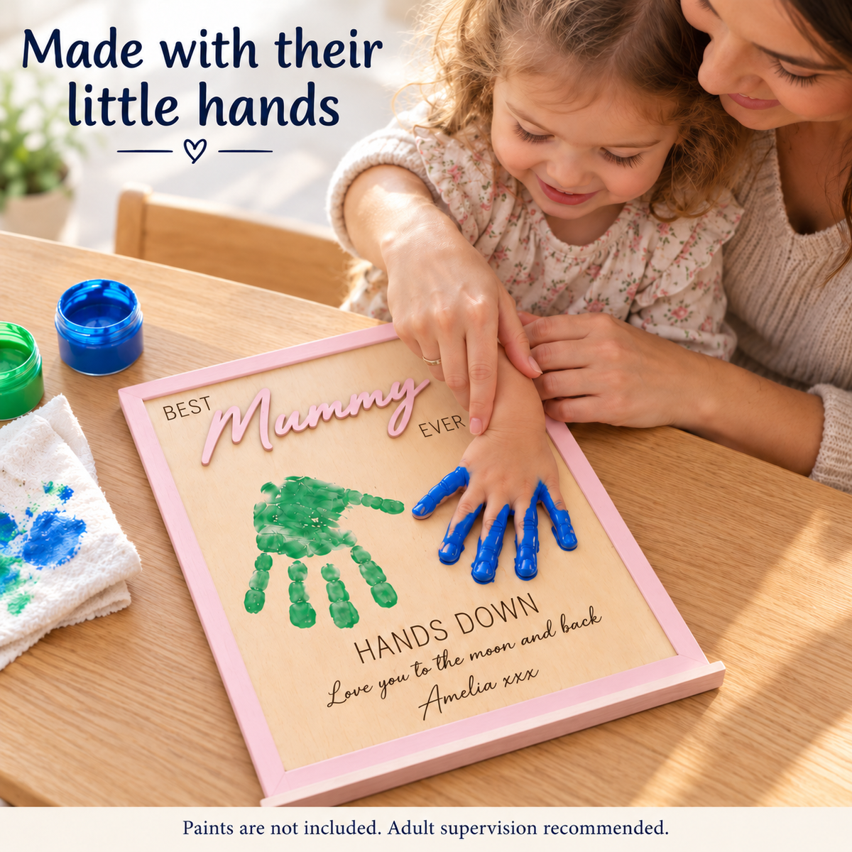 Child and mother creating paint handprints on a pastel pink Mummy wooden frame; paints are not included.