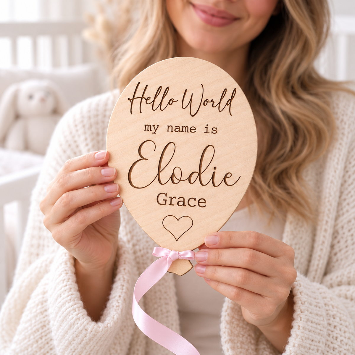 Parent holding a personalised Hello World wooden balloon plaque with Elodie Grace engraved and a pink satin ribbon.
