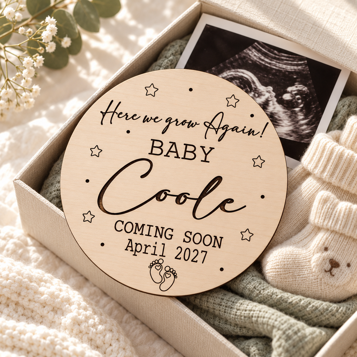 Engraved Here We Grow Again pregnancy keepsake in a linen box beside an ultrasound and baby socks