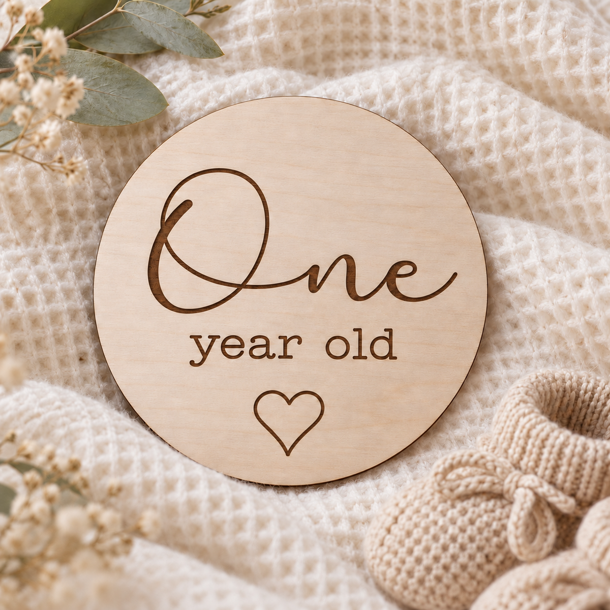 One year old wooden photo card with script lettering and an outline heart on an ivory blanket