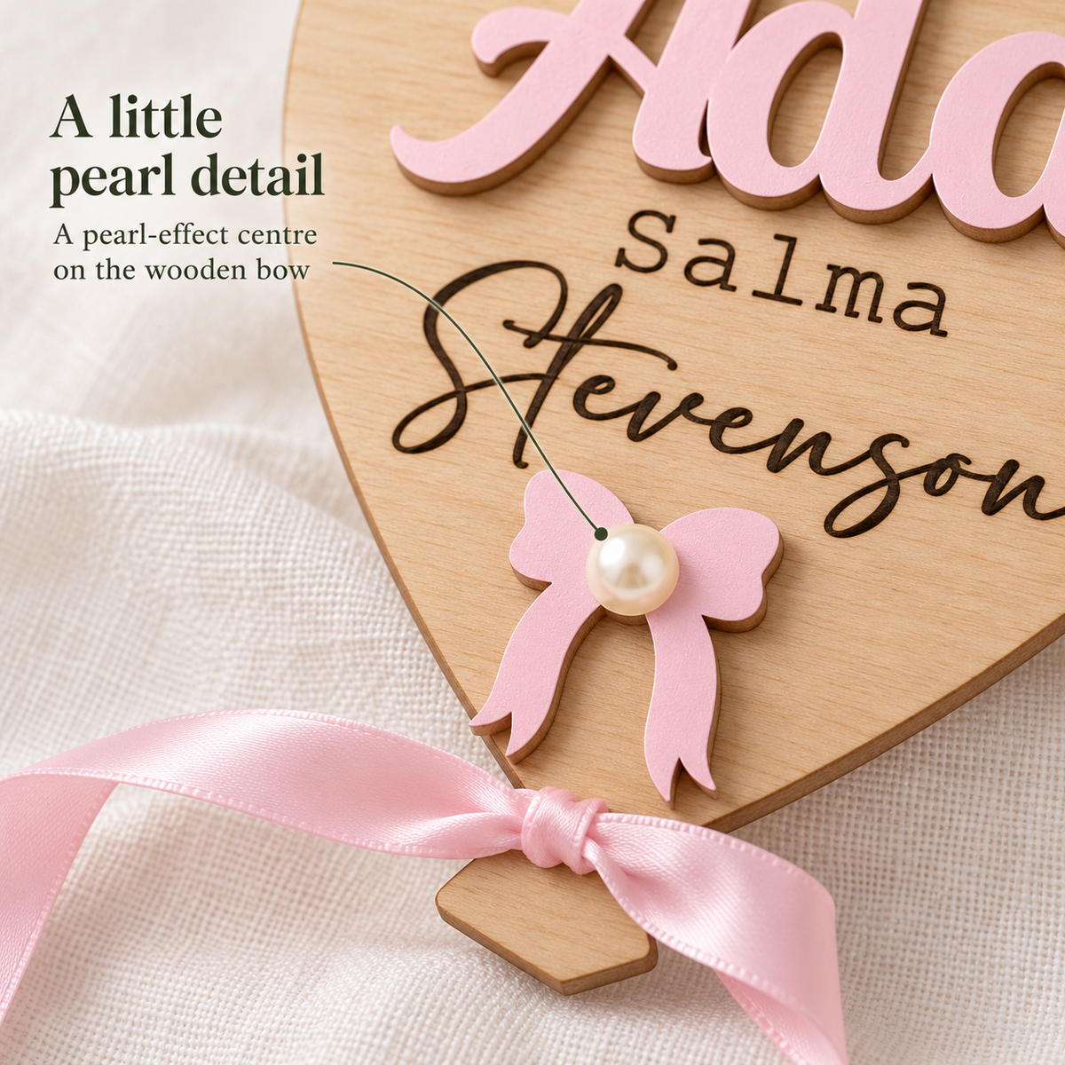 Close-up of the painted wooden bow and single pearl-effect centre on the personalised balloon plaque.