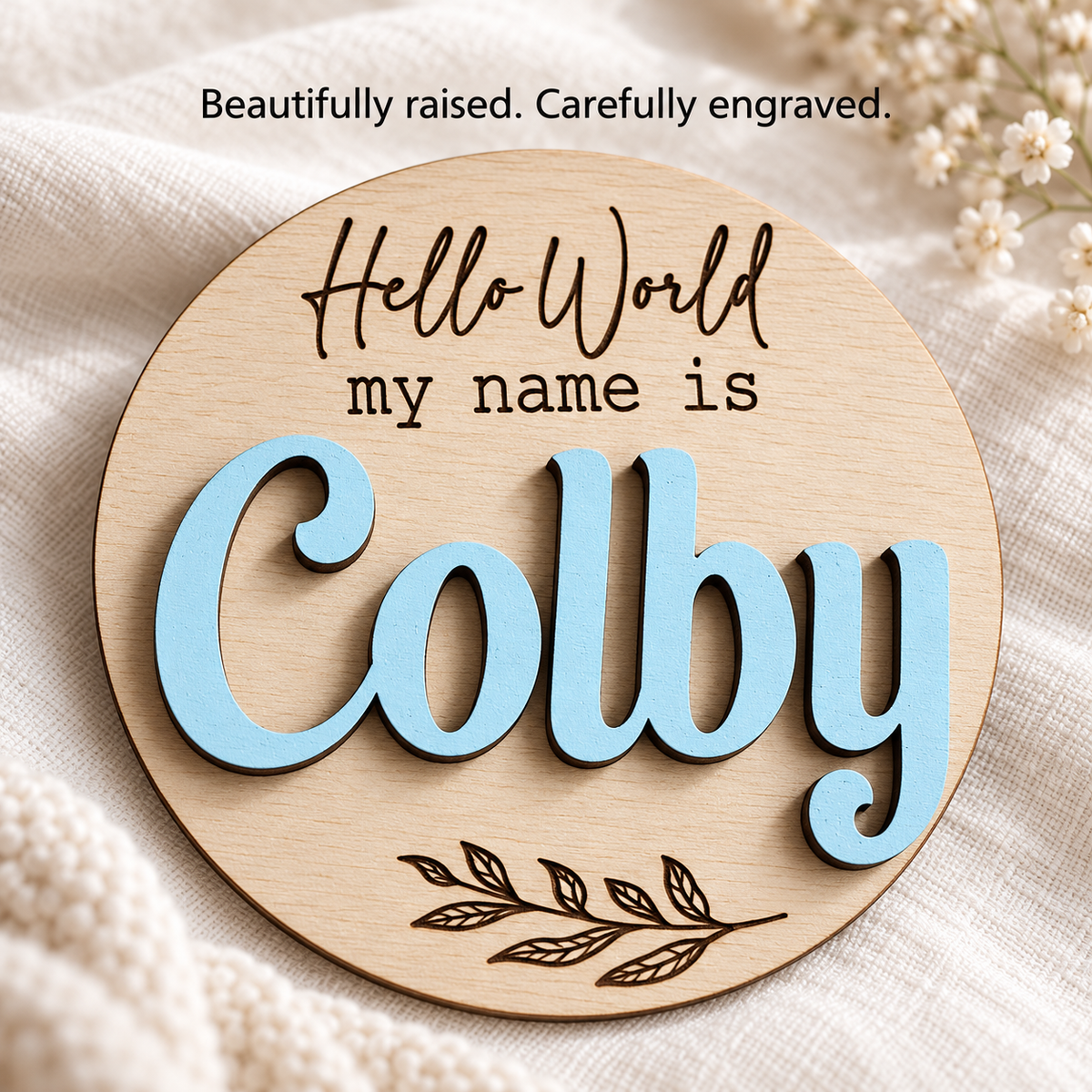 Close-up of raised Pastel Blue Colby lettering and dark engraving on a personalised wooden baby name disc.