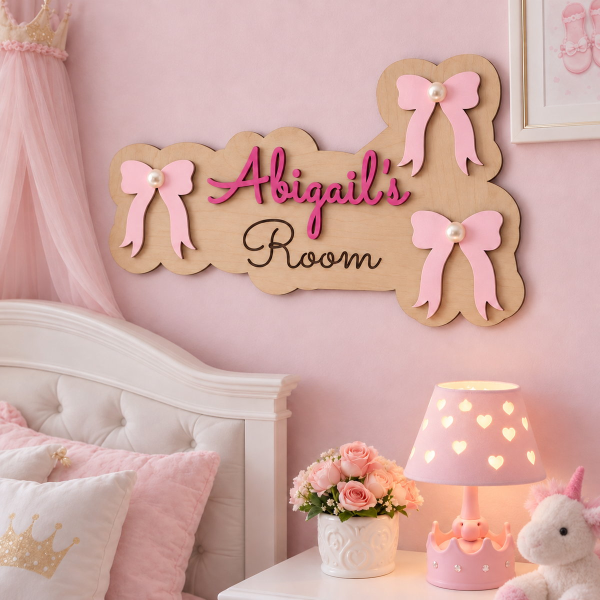 Abigail's Room wooden bow door sign on a pink bedroom wall, with clear spacing between the left bow and raised dark pink name.