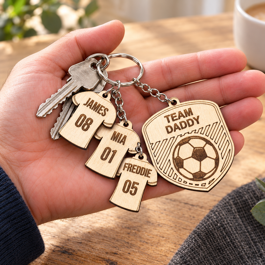 Personalised wooden football keyring in a hand, with Team Daddy badge and James 08, Mia 01 and Freddie 05 shirt charms