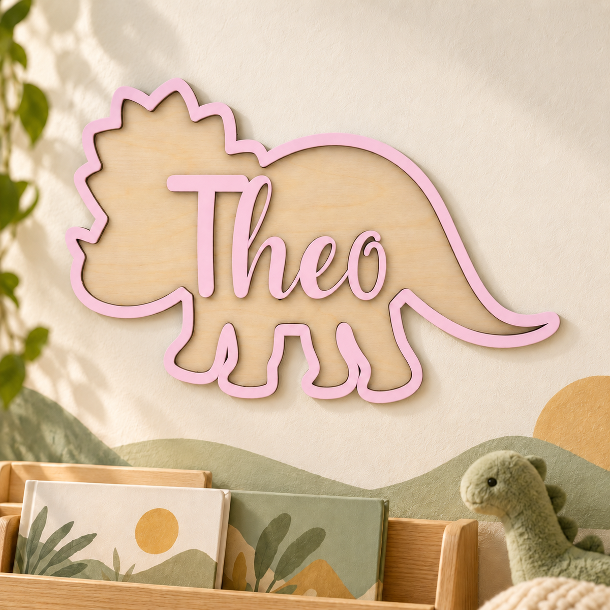 Pastel pink personalised wooden triceratops name sign with raised Theo lettering in a dinosaur themed reading nook.