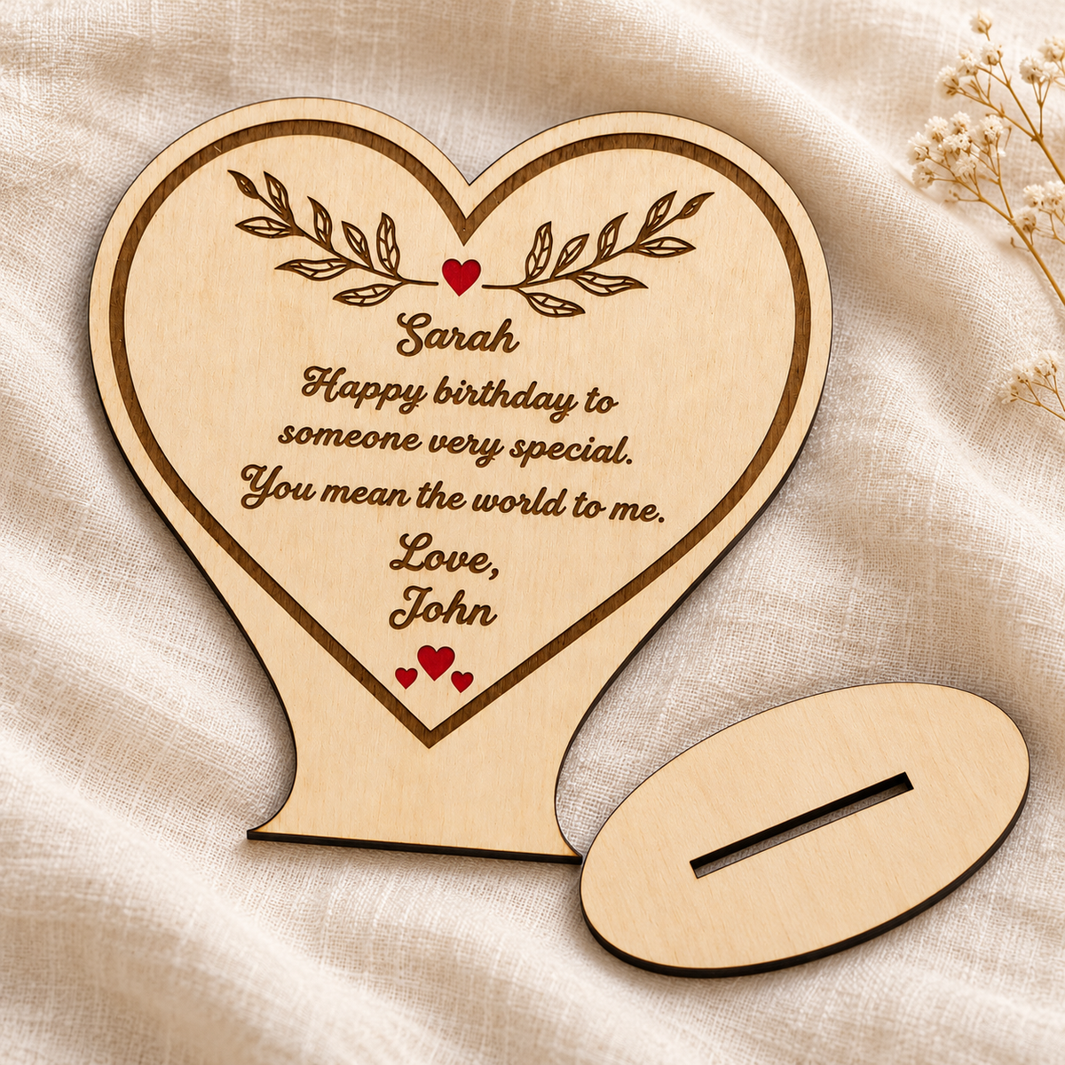 Personalised wooden heart lying on linen beside its separate oval display stand