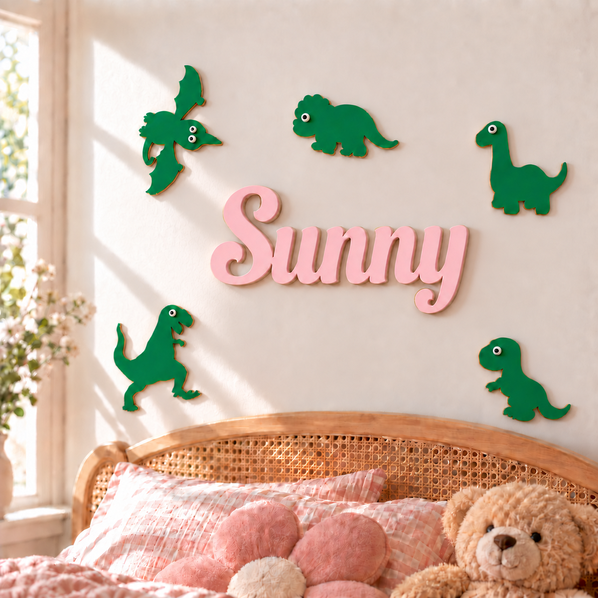 Smaller connected pink Sunny wooden name with five green dinosaur decorations above a rattan bed in a girl's bedroom