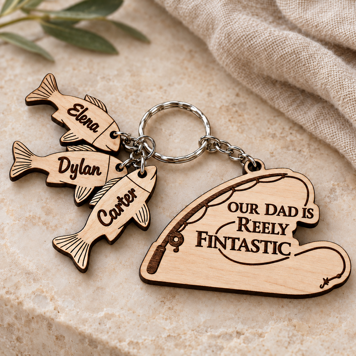 Our Dad is Reely Fintastic personalised fishing keyring with Carter, Elena and Dylan wooden fish charms on a stone background