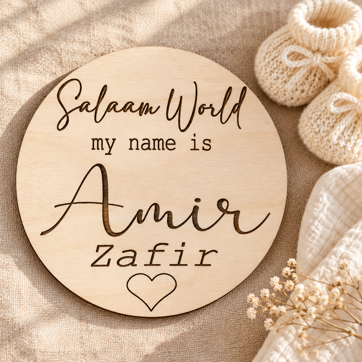 Engraved Salaam World baby name disc styled with newborn booties and a soft blanket for a first photograph