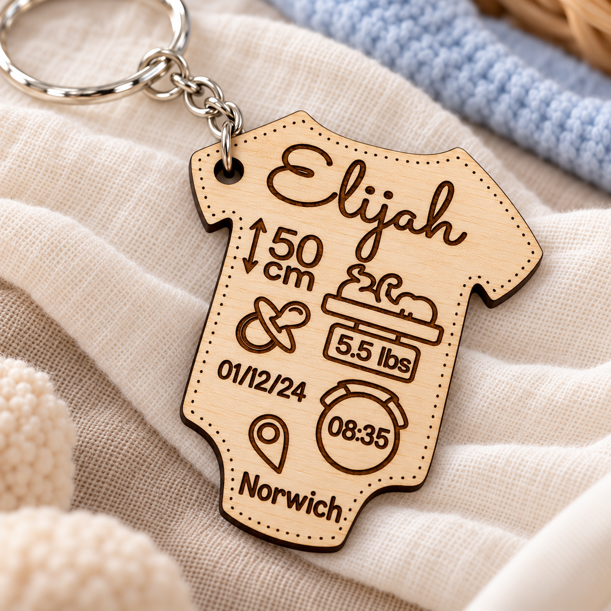 Close-up of engraved baby birth details and natural birch grain on a baby vest keyring