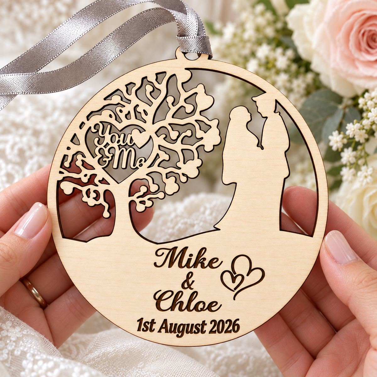 Personalised birch wedding and anniversary hanging ornament held in hands, showing the open tree and couple design and dark engraved names.