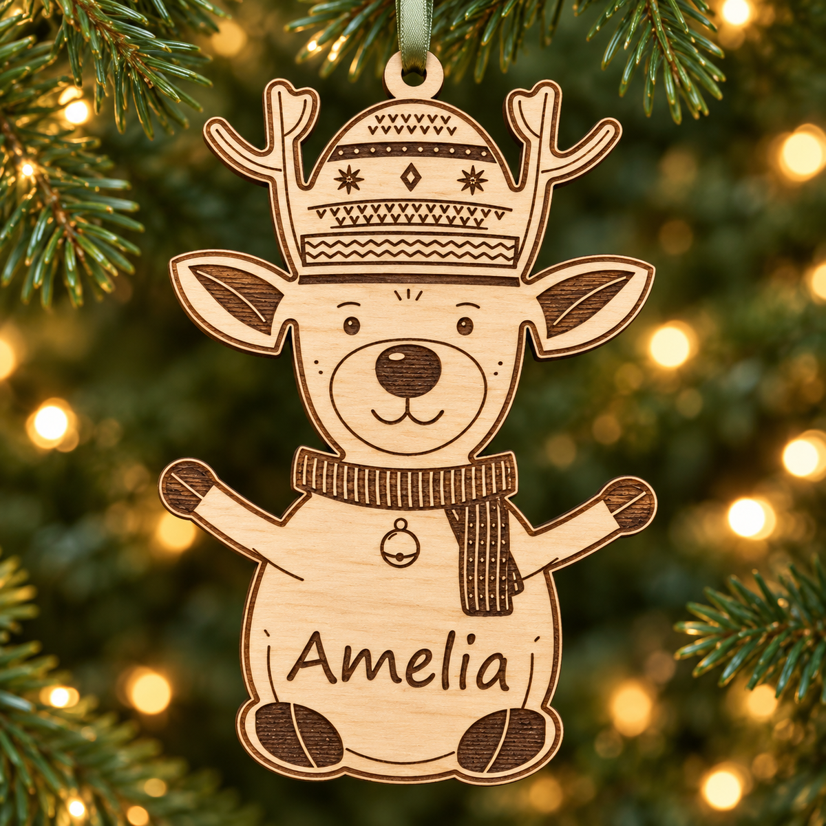 Personalised wooden reindeer bauble engraved with Amelia, hanging on a Christmas tree from a sage green satin ribbon.