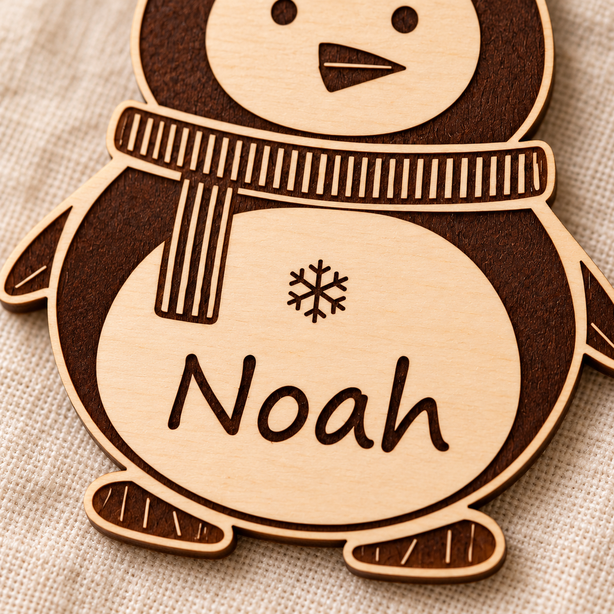 Close-up of the Noah name and snowflake engraved into the pale birch belly of a wooden penguin ornament