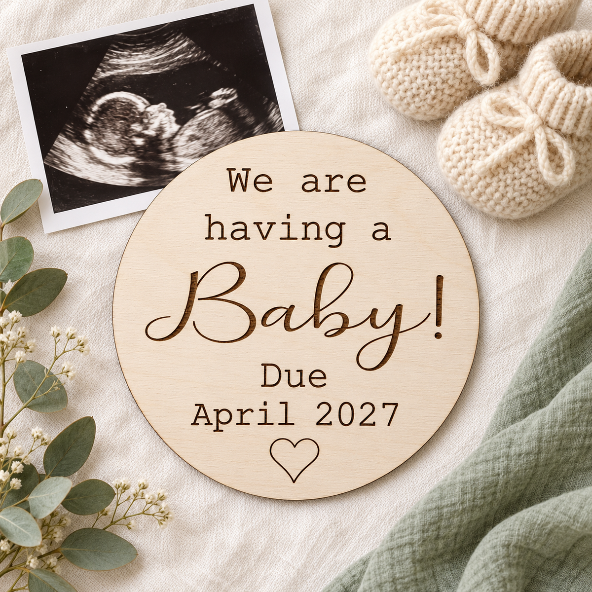We are having a Baby due date plaque beside a scan print and knitted baby booties on ivory and sage fabric