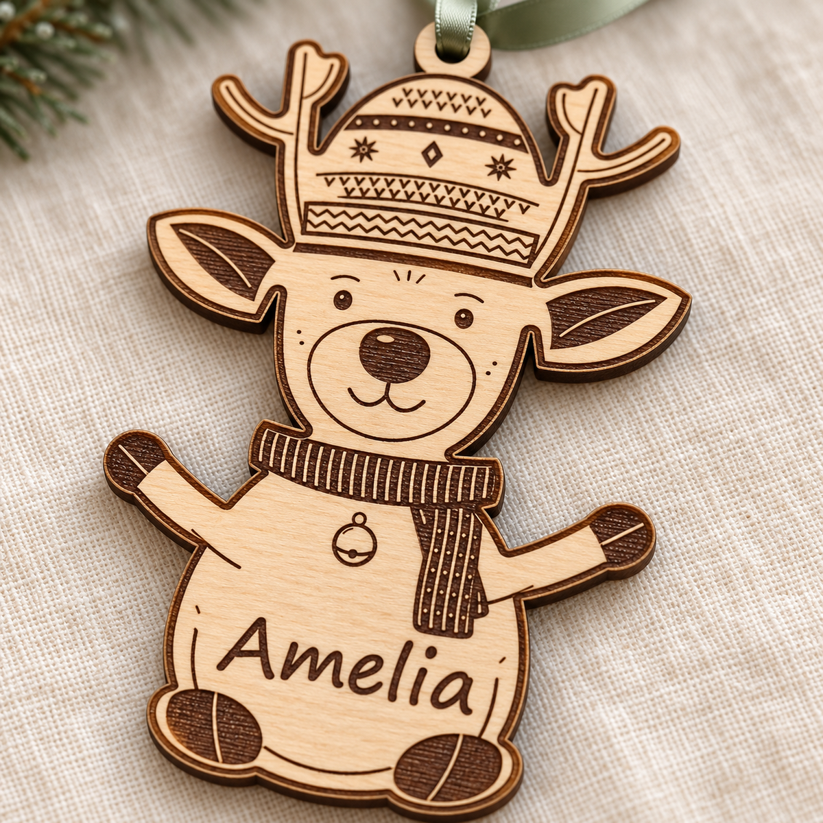 Close-up of the Amelia name, striped scarf, bell and hoof details laser engraved into the birch plywood reindeer ornament.
