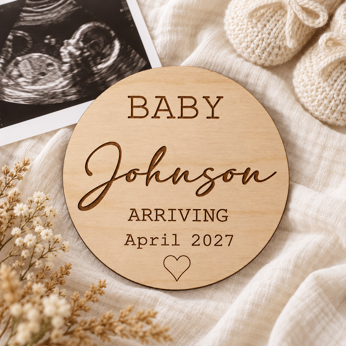 Baby Johnson Arriving April 2027 wooden sign beside a scan photo and knitted booties