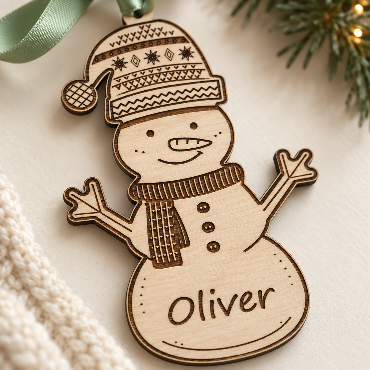 Close-up of the snowman's engraved hat, scarf and Oliver name, showing the natural wood grain and cut edge.