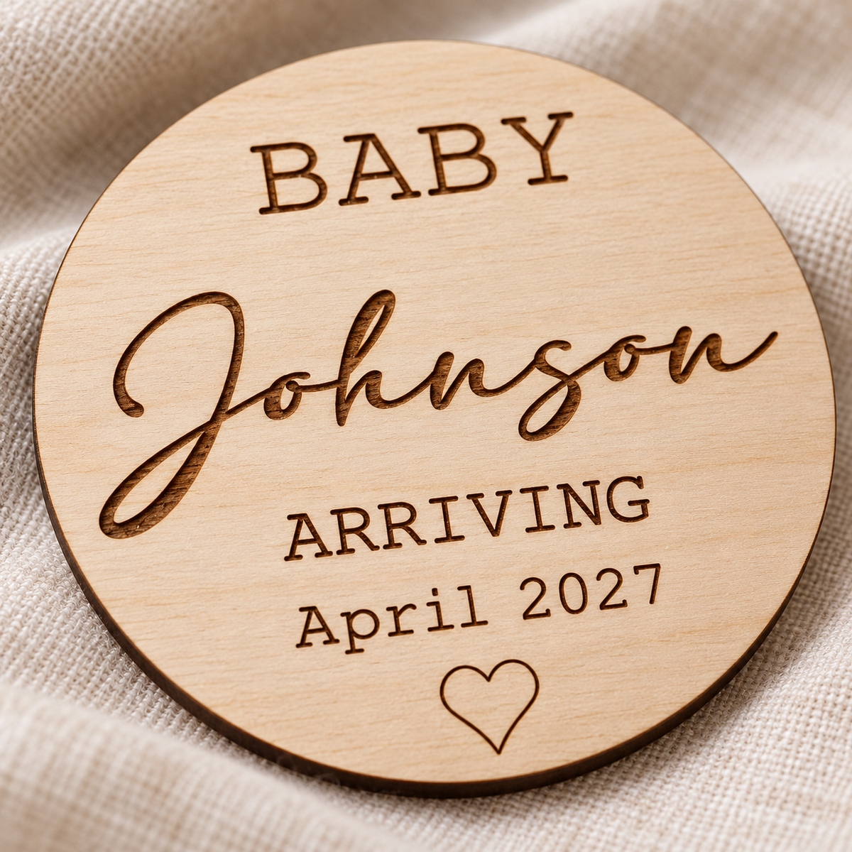 Close-up of dark laser engraved surname, due date and heart on birch plywood