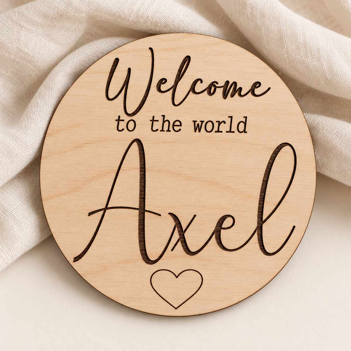 Round natural birch Welcome to the World sign with engraved Axel name and heart on an ivory linen background