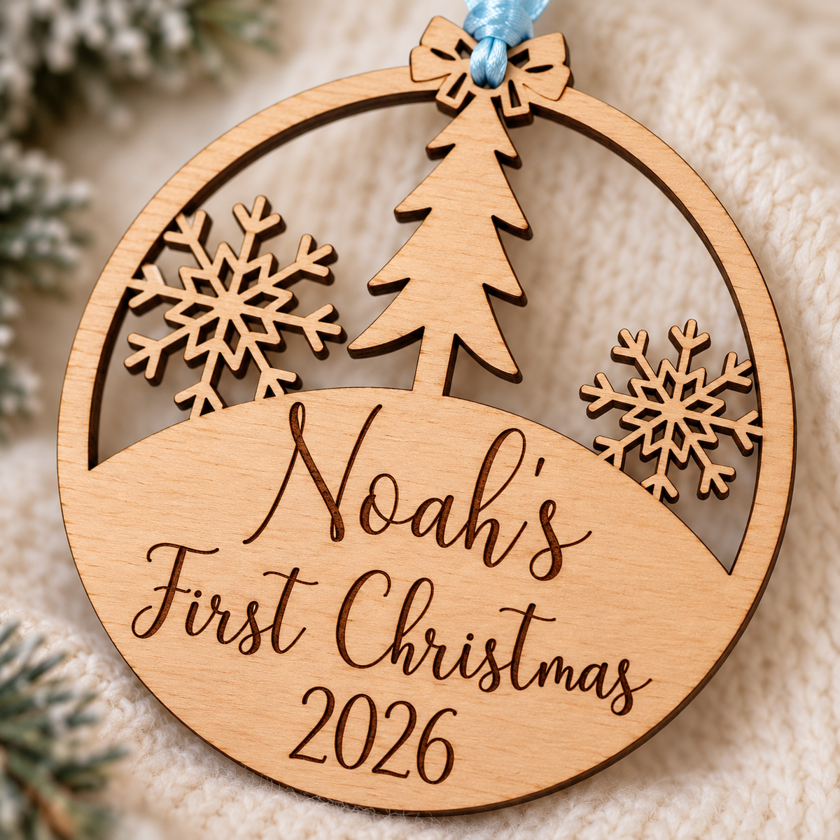 Close-up of dark laser-engraved Noah's First Christmas 2026 lettering, natural birch grain and the ornament's tree and snowflake cut-outs