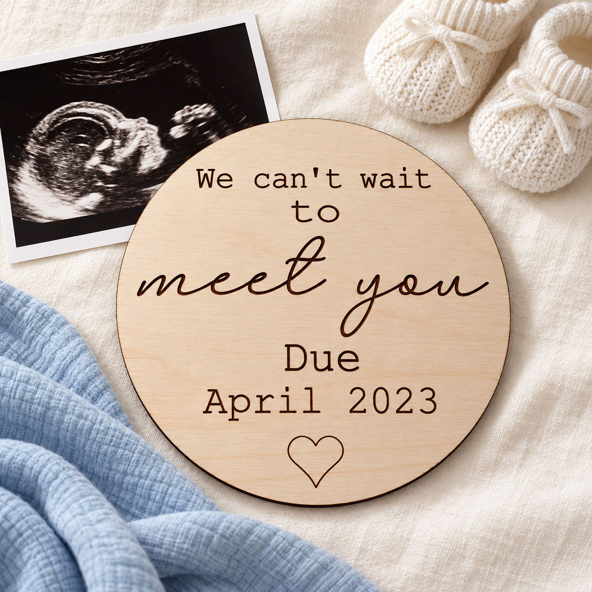 Can't Wait to Meet You pregnancy announcement plaque styled with an ultrasound photo, cream baby booties and blue muslin.