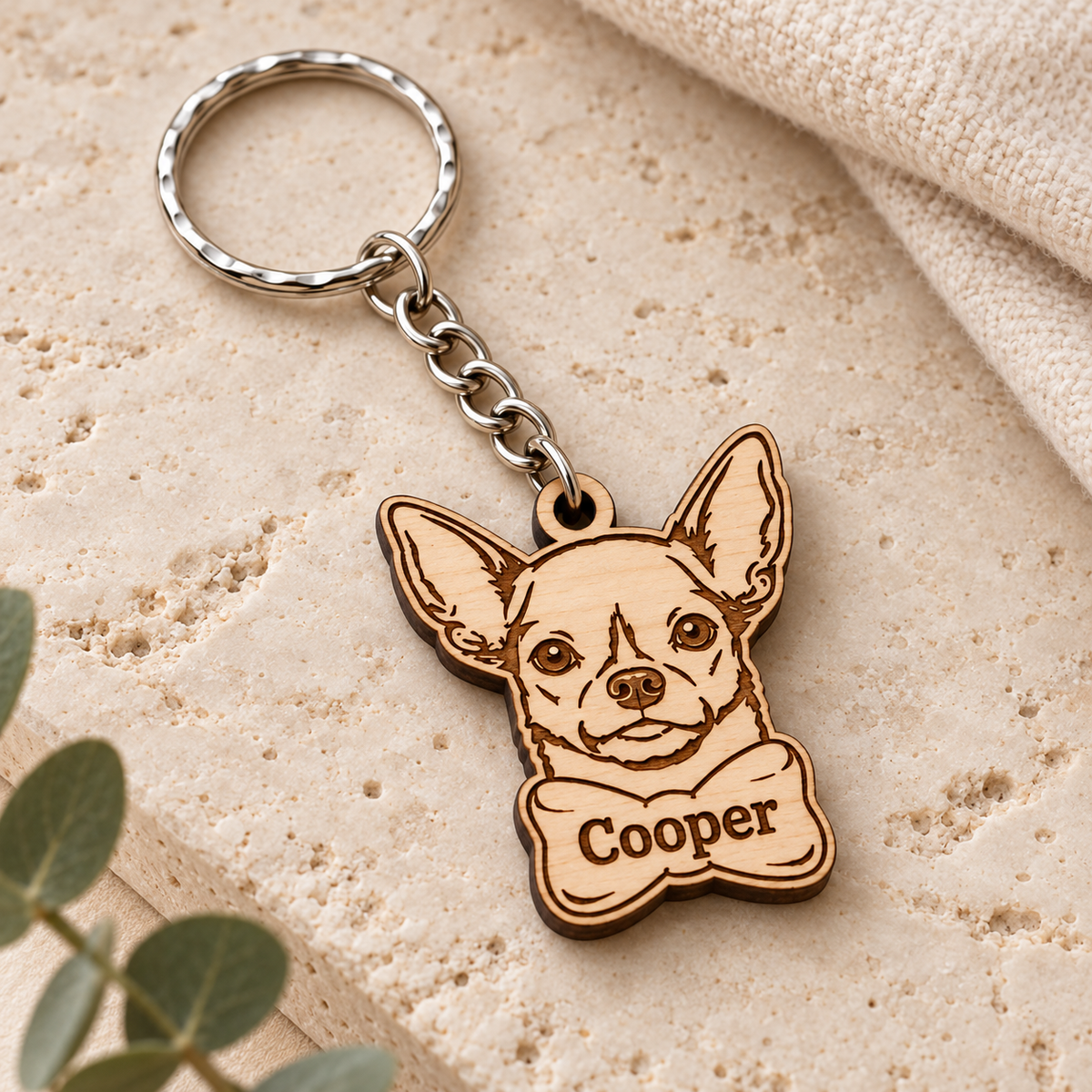 Close-up of Cooper bottom bow Chihuahua keyring showing engraved face details and natural wooden finish on cream travertine