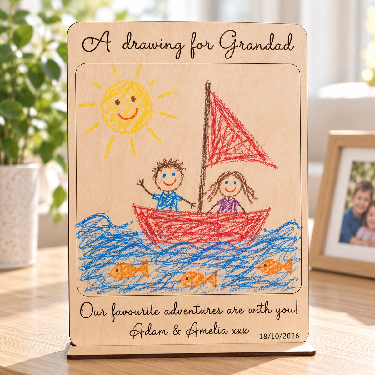 Personalised wooden drawing gift for Grandad displayed on its stand, with a child's crayon sailing boat picture, names and date.