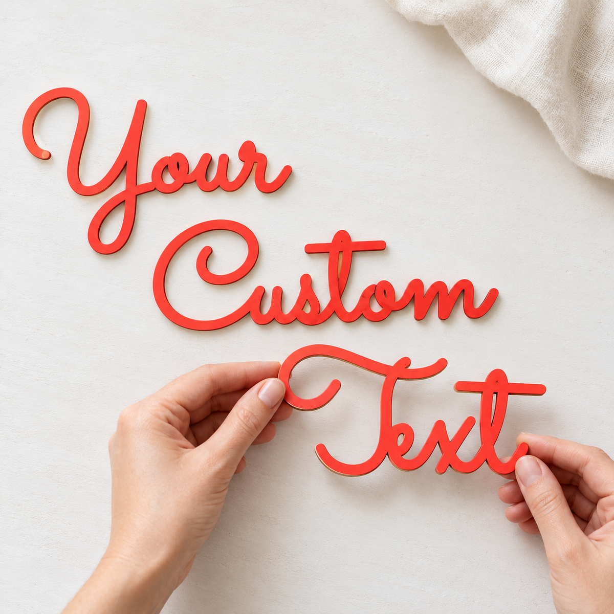 Coral red Your Custom Text wooden word cutouts on a white surface, with hands holding the final word.
