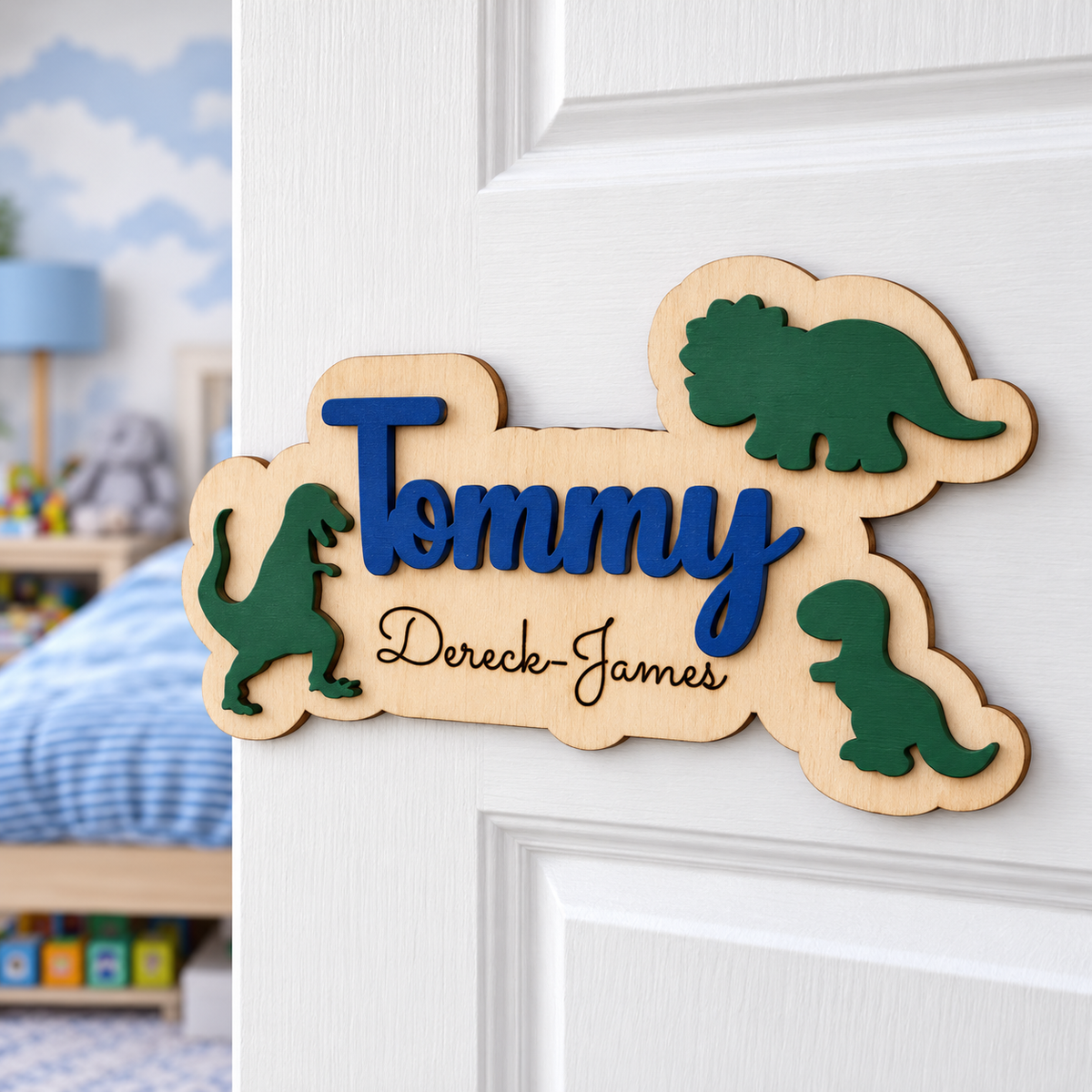 Personalised dinosaur bedroom door sign with navy Tommy lettering, black Dereck-James engraving and three green dinosaurs on a white door.