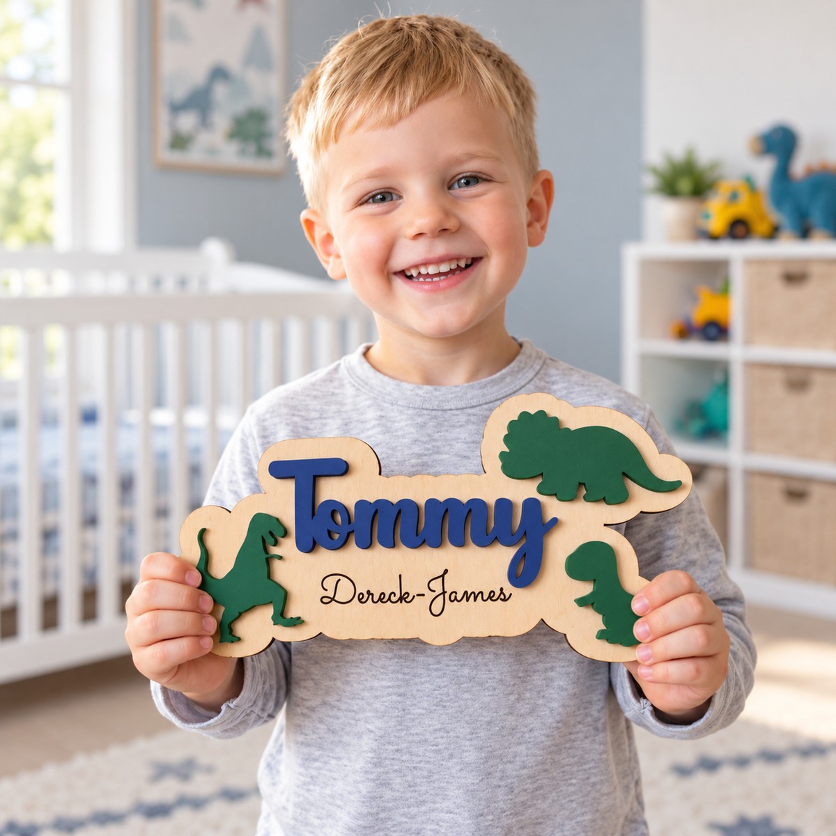 Smiling child holding a wooden dinosaur plaque with navy Tommy name and black engraved Dereck-James underneath.