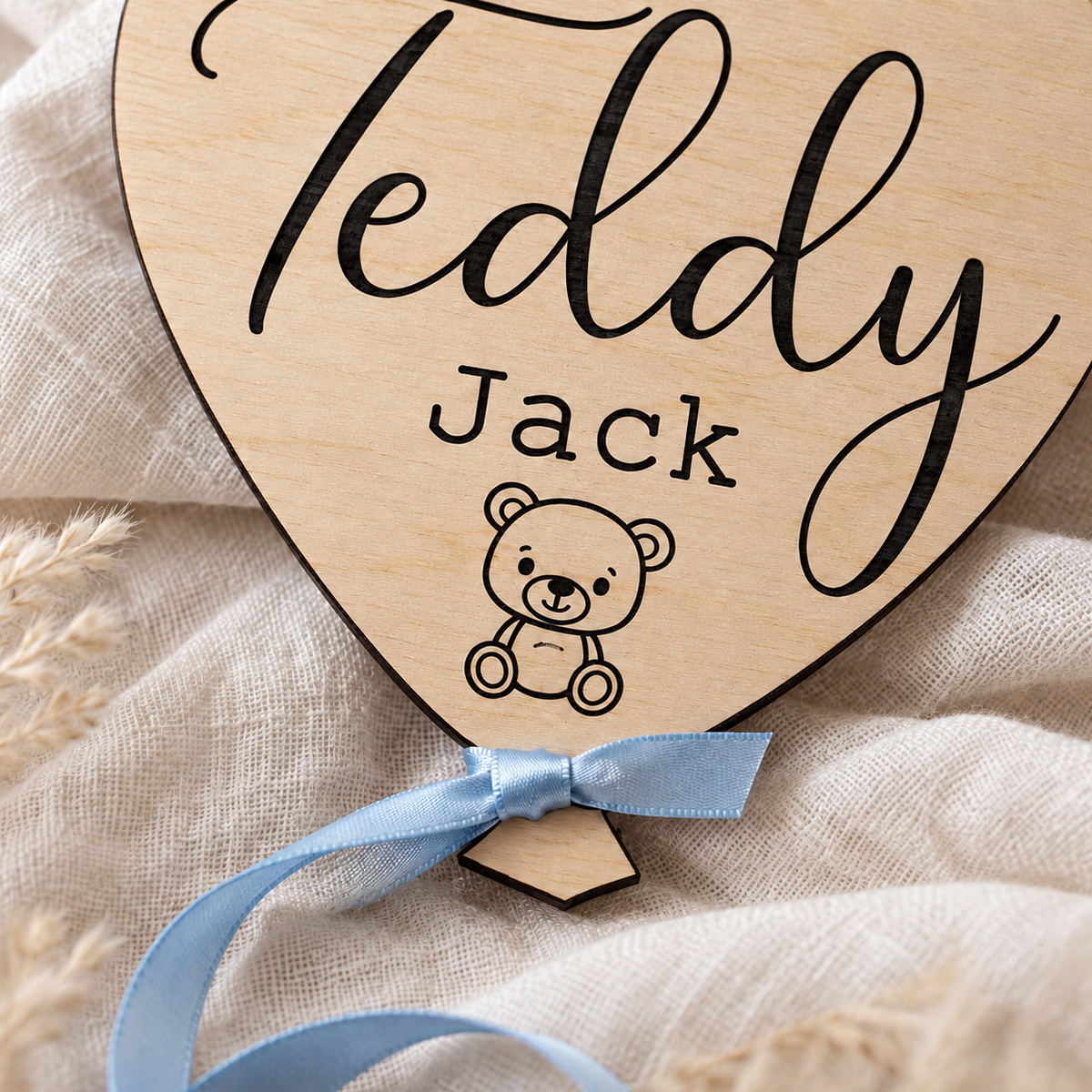 Close-up of dark laser engraving, teddy bear illustration and blue ribbon on birch plywood