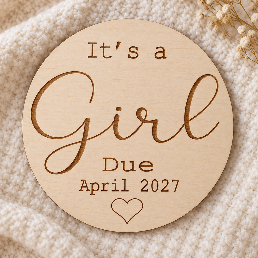 It's a Girl engraved birch gender reveal sign with April 2027 due date on a cream blanket