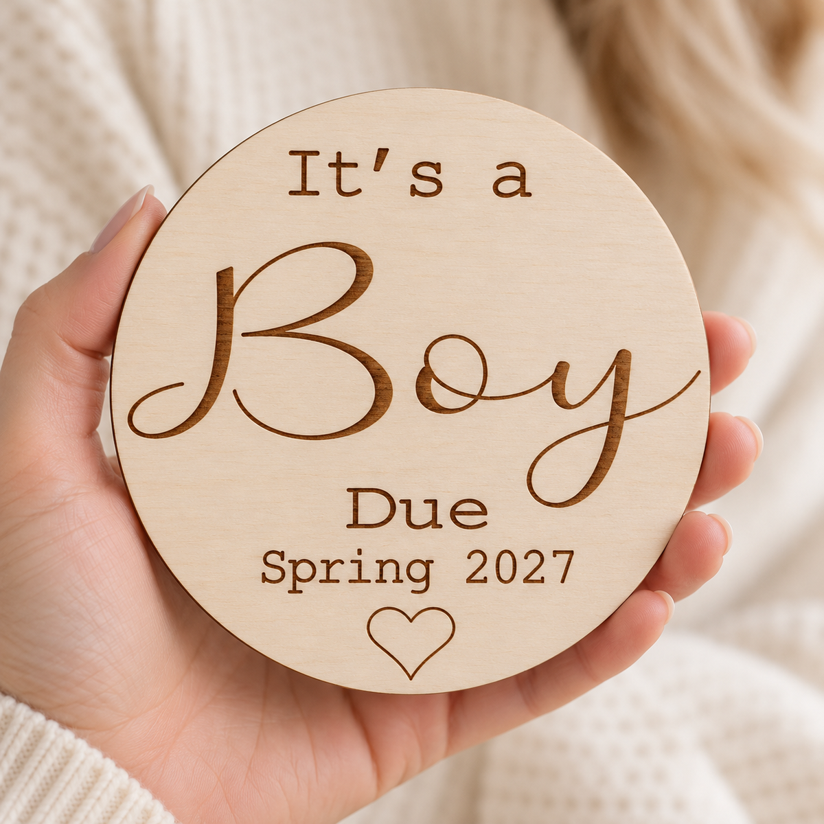 It's a Boy due date plaque held in one hand against a warm neutral background