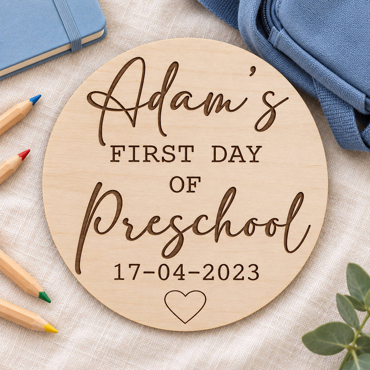 Personalised first day of Preschool sign with dark engraving beside pencils and a blue school bag
