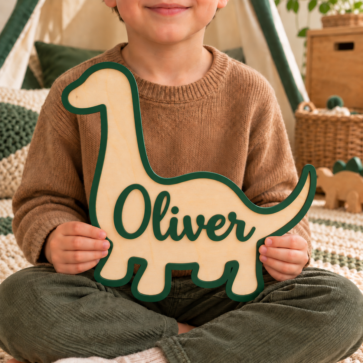 Child holding a forest green brachiosaurus name sign with raised Oliver lettering and a natural birch base